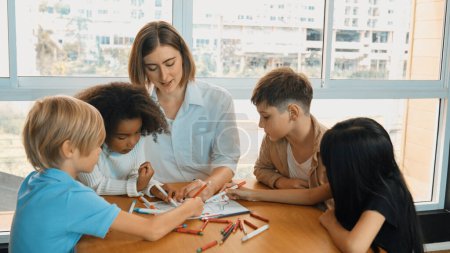 Photo for Professional caucasian teacher telling story to diverse student while sitting at table with storybook and colored book. Smart learner listening story while colored picture from instructor. Erudition. - Royalty Free Image