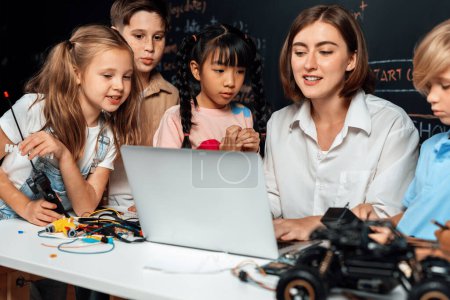 Photo for Teacher coding to demonstrate children how to code robots in the STEM class. Children fun to watch how teacher coding with confident only boy in blue shirt taking note with serious look. Erudition. - Royalty Free Image
