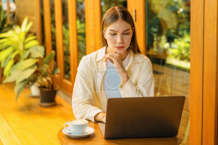 Young woman working on laptop at outdoor cafe garden during springtime, enjoying serenity ambient at coffee shop. Digital nomad freelancer or college student working remotely or blogging. Expedient