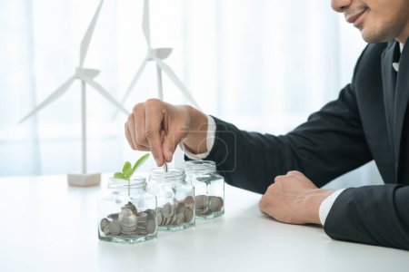 Geschäftsmann legte Münze in Geld sparendes Glas in seinem Büro als nachhaltige Geldanlage oder Öko-Subvention. Grüne Unternehmen fördern und investieren das Umweltbewusstsein. Kreisel