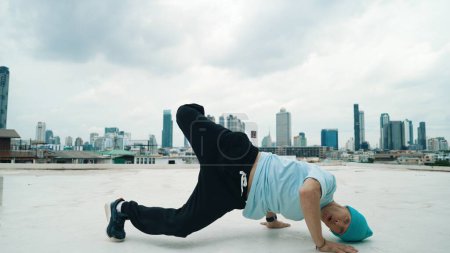 Photo for Caucasian B-boy dancer practicing street dancing at rooftop with city or urban. Motion shot of young man performing street dance by doing freeze pose or doing hand stand. Outdoor sport 2024. Endeavor. - Royalty Free Image