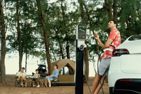 Photo for Outdoor adventure and family vacation camping in nature travel by eco friendly car for sustainable future. Lovely sit on trunk, charging EV car with EV charging station in campsite. Perpetual - Royalty Free Image