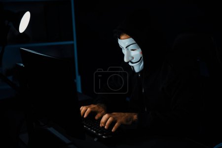 Foto de Blanco sonriente máscara anónima criminal instalar la programación de cifrado de virus por la aplicación hacker en el sistema de servidor de datos en la privacidad en el rescate de la computadora. Búsqueda de información en el ordenador. Conjetura. - Imagen libre de derechos