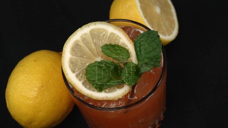 Makrographie eines Tequila Sunrise Cocktails, geschmückt mit einer Zitronenscheibe und frischem Minzblatt, vor einem dramatischen schwarzen Hintergrund. Nahaufnahme fängt die lebhaften Farben des Cocktails ein. Komestibel.