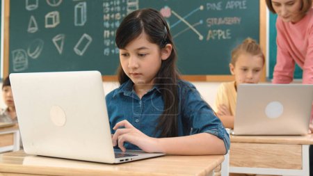 Photo for Cute girl looking at laptop screen while coding engineering prompt. Multicultural student learning about generated AI while teacher teaching about system or checking classwork at STEM class. Pedagogy. - Royalty Free Image