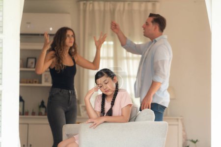 Photo for Annoyed and unhappy young girl sitting on sofa trapped in middle of tension by her parent argument in living room. Unhealthy domestic lifestyle and traumatic childhood develop to depression.Synchronos - Royalty Free Image