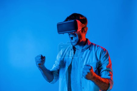 Photo for Happy excited man watching at sport competition at virtual world while wearing VR headset at neon light background. Handsome teenager enter future innovation technology by using goggles. Deviation. - Royalty Free Image