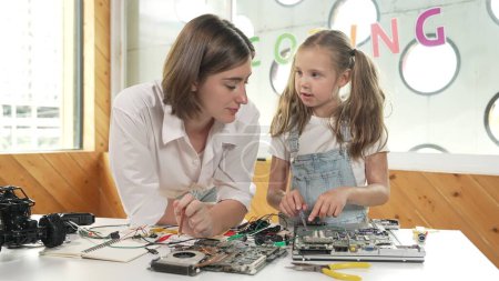 Photo for Young smart caucasian teacher teaching students about part of electronic board. Expert girl learn about digital electrical tool and fixing motherboard at table with chips and wires placed. Erudition. - Royalty Free Image