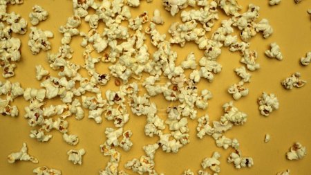 Slow motion shot of popcorn was throwing with yellow background. Fresh movie popcorn moving and falling. Popcorn in motion falling in a captivating dance. Dynamic movement and energy. Comestible.