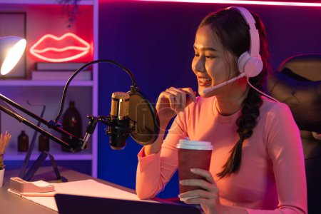 Photo for Host channel of creative broadcast listening the music on social media with listeners holding coffee up, wearing pastel color headphones, using mic radio record by camera at neon studio. Stratagem. - Royalty Free Image