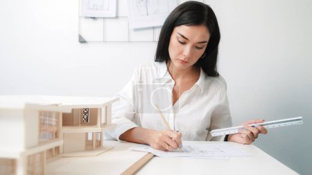 Closeup portrait image of professional young beautiful engineer architect using triangular scale measures house model with focusing at modern office. Business creative design concept. Immaculate.