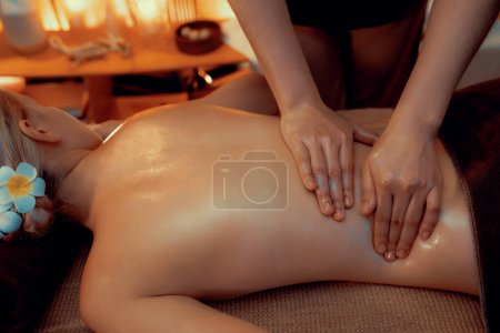 Photo for Closeup woman customer enjoying relaxing anti-stress spa massage and pampering with beauty skin recreation leisure in warm candle lighting ambient salon spa at luxury resort or hotel. Quiescent - Royalty Free Image