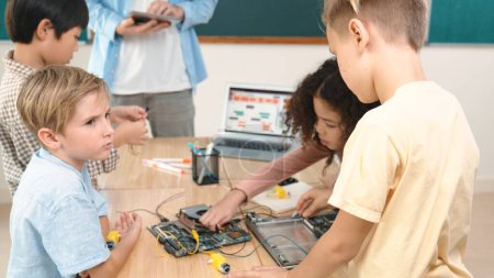 Photo for Cute energetic children working on electronic board while teacher using tablet analyze data. Group of diverse student fixing main board and learning about generated AI and programing system. Pedagogy. - Royalty Free Image