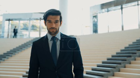 Photo for Portrait of Serious business man looking at camera while standing at stairs. Closeup of successful man staring at camera while wearing business suit. Happy executive manager look at camera. Exultant. - Royalty Free Image