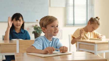 Photo for Smart elementary student looking at teacher while attend in classroom. Diverse smart student sitting at classroom while listening teacher explain about classwork or test. Education concept. Pedagogy. - Royalty Free Image