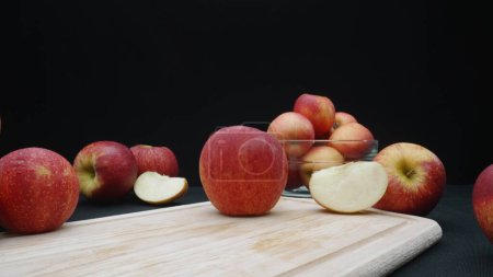 Makrographie von Äpfeln in verschiedenen Formen: ganz, in Scheiben geschnitten und in einer Glasschale mit schwarzem Hintergrund. Jede Nahaufnahme fängt die roten Farben der Äpfel auf dem Schneidebrett ein. Komestibel.