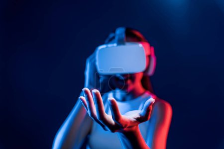 Photo for Smart Female standing surrounded by neon light wear VR headset connecting metaverse, futuristic cyberspace community technology. Elegant woman use hand holding generated virtual object. Hallucination. - Royalty Free Image
