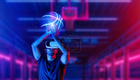 Téléchargez les photos : Personne de sport caucasienne jouant au basket au stade de sport néon tout en portant un tissu décontracté et des lunettes de réalité virtuelle. Athlète tenant un hologramme de basket-ball alors qu'il se tenait debout à l'arène sportive. Déviation. - en image libre de droit