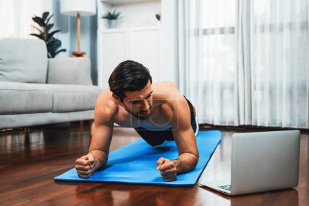 Photo for Athletic and sporty man doing plank on fitness mat during online body workout exercise session for fit physique and healthy sport lifestyle at home. Gaiety home exercise workout training. - Royalty Free Image