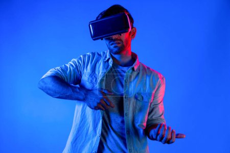 Téléchargez les photos : Homme intelligent caucasien portant du verre VR et geste mobile tenant pistolet. Gamer utilisant un futur casque de réalité virtuelle numérique ou une innovation futuriste pour entrer dans le méta-monde ou jouer à un jeu d'action. Déviation. - en image libre de droit