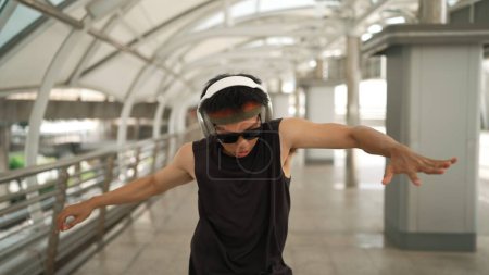 Photo for Closeup of smart handsome dancer moving hands while dance to hip hop music. Asian hipster wearing headphone while walking along the corridor with blurring background. Outdoor sport 2024. Sprightly. - Royalty Free Image