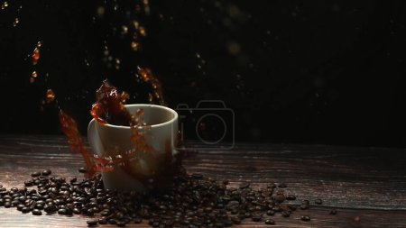 Téléchargez les photos : Mouvement super lent de chute de glace tombant dans la tasse de café et éclaboussures avec fond noir séparé. Gros plan de la goutte de sucre dans l'espresso entouré d'une pile de grains de café. Coup de feu. Comestible. - en image libre de droit