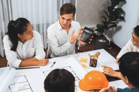Photo for Diverse group of civil engineer and client working together on architectural project, building blueprint and calculate risk reduction for construction project at meeting table. Prudent - Royalty Free Image