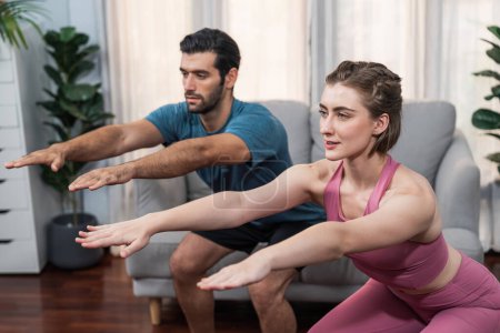 Athletic and sporty couple doing squat together during home body workout exercise session for fit physique and healthy sport lifestyle at home. Gaiety home exercise workout training concept.