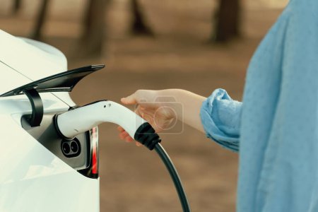 Branchez le chargeur EV à la main dans le véhicule électrique pour recharger la batterie de voiture EV de la station de charge extérieure. Environnement de jour frais avec concept alternatif d'énergie propre et durable. Perpétuel