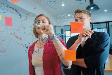 Photo for Couple of young creative start up business people brainstorming idea and solving problems by using sticky note and mind map at glass board, meeting room. discussing, working together. Immaculate. - Royalty Free Image