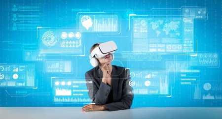 Téléchargez les photos : Femme d'affaires caucasienne avec lunettes VR tout en regardant hologramme de graphique financier. Gestionnaire de projet professionnel assis tout en pensant et en prenant une décision lors du codage du programme. Machines et appareils. - en image libre de droit