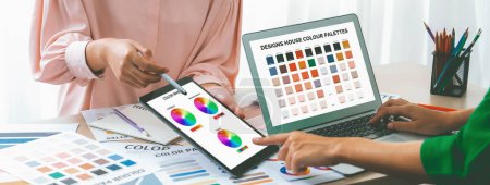 A cropped picture of professional designer selects the color by using color theory while using laptop compare the color on table with designing material and equipment scatter around. Variegated.