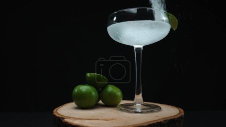 Macrography, eine verlockende Margarita, wird in einem Glas eingefangen, das mit einer lebendigen Limettenscheibe garniert ist, alles vor einem fesselnden schwarzen Hintergrund. Jede Nahaufnahme von Cocktail und Limette. Komestibel.