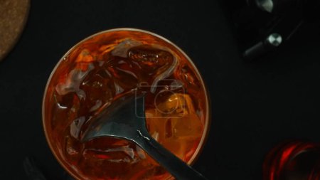 Macrografía, experimente el arte de mezclar un cóctel Negroni desde una perspectiva de arriba hacia abajo, adornado con una rebanada de naranja fresca y vibrante, todo sobre un fondo negro dramático. Vista de arriba abajo. Comestible.