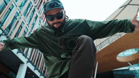 Photo for Low angle view of hipster pose in hip hop style surrounded by mall view. Portrait of sporty asian hip hop choreographer dancing break dance while looking at camera. Outdoor sport 2024. Endeavor. - Royalty Free Image