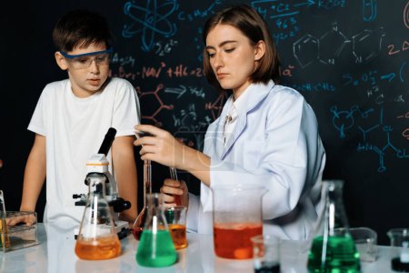 Photo for Teacher support schoolboy in laboratory. Schoolboy and teacher stand and experiment about science of chemistry in STEM class using liquid in glass container. Instructor mixing solution. Erudition. - Royalty Free Image