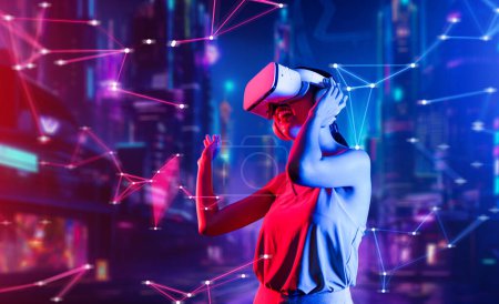Foto de Mujer de pie en realidad virtual estilo cyberpunk edificio desgaste VR auriculares que conectan metaverso, tecnología futura comunidad del ciberespacio, Mujer bailando levantando un brazo sosteniendo gafas. Alucinaciones. - Imagen libre de derechos