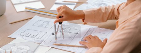 Photo for Professional architect drawing blueprint by using divider on the table with stationary and architectural document scatter around at architectural office. Closeup. Focus on hand. Delineation. - Royalty Free Image