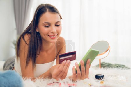 Photo for Young woman lying on the bed using online payment app and digital wallet on smartphone to pay with credit card. E commerce shopping and modern purchasing via mobile internet. Unveiling - Royalty Free Image