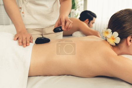 Téléchargez les photos : Massage aux pierres chaudes au salon de spa dans un complexe de luxe avec une lumière du jour sérénité ambiante, un couple heureux client profitant d'un massage aux pierres de basalte spa glisse sur le corps avec une chaleur apaisante. Tranquillité - en image libre de droit