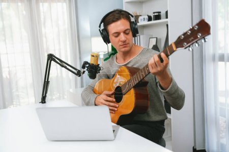 Photo for Host channel in smart singer with smiling face, playing guitar along singing, broadcasting on social media channel, wearing headphones to record video streamer at modern studio recording. Pecuniary. - Royalty Free Image