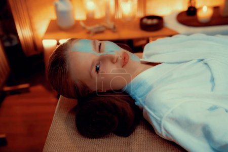 Photo for Serene ambiance of spa salon, woman customer smiling and rejuvenating with luxurious face cream massage with warm lighting candle. Facial skin treatment and beauty care concept. Quiescent - Royalty Free Image