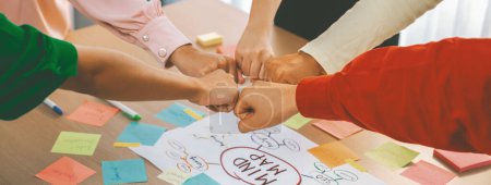 Photo for Young happy creative startup group join circle fist bump hands together surrounded by marketing strategy mind map and colorful sticky notes at meeting room. Unity and teamwork concept. Variegated. - Royalty Free Image