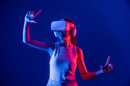 Photo for Female stand surrounded by neon light wear VR headset connecting metaverse, futuristic cyberspace community technology, spread both hand index and thumb finger interact virtual object. Hallucination. - Royalty Free Image