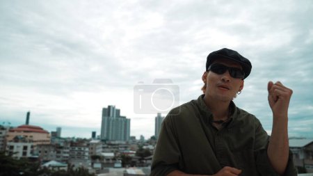 Photo for Closeup image of hipster put hands up at rooftop while looking at camera. Portrait of hip-hop dancer or choreographer looking at camera with confident surround with city. Outdoor sport 2024. Endeavor. - Royalty Free Image