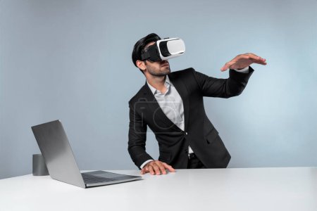 Photo for Professional project manager looking by using VR goggle while sitting at laptop. Skilled business man wearing visual reality headset while connecting metaverse or visual world. Innovation. Deviation. - Royalty Free Image