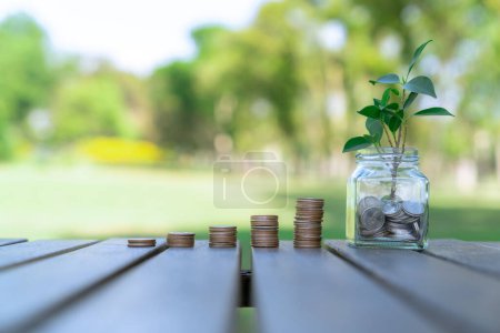 El concepto de inversión sostenible en crecimiento monetario con frasco de vidrio lleno de ahorros de dinero y pila de monedas representa una inversión financiera ecológica alimentada con la naturaleza. Gyre.