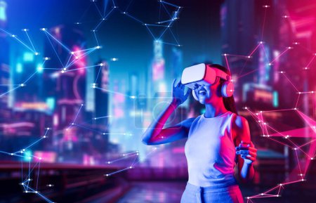 Photo for Female standing in cyberpunk style building in meta wear VR headset connecting metaverse, future cyberspace community technology. Woman touching goggle looking far virtual construction. Hallucination. - Royalty Free Image