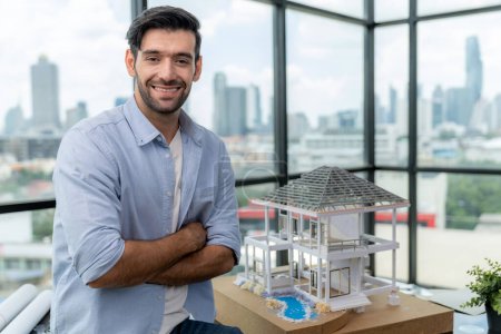 Photo for Portrait of architect engineer in casual outfit smile at camera while crossing arms. Businessman looking at camera and standing with arms folded near house model, architectural model. Tracery. - Royalty Free Image