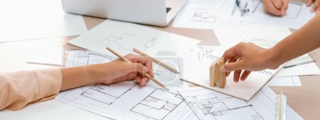 Photo for Professional architect hand draws a blueprint on table with architectural document and wooden block scatter around at office. Design and Planing concept. Focus on hand. Closeup. Delineation. - Royalty Free Image